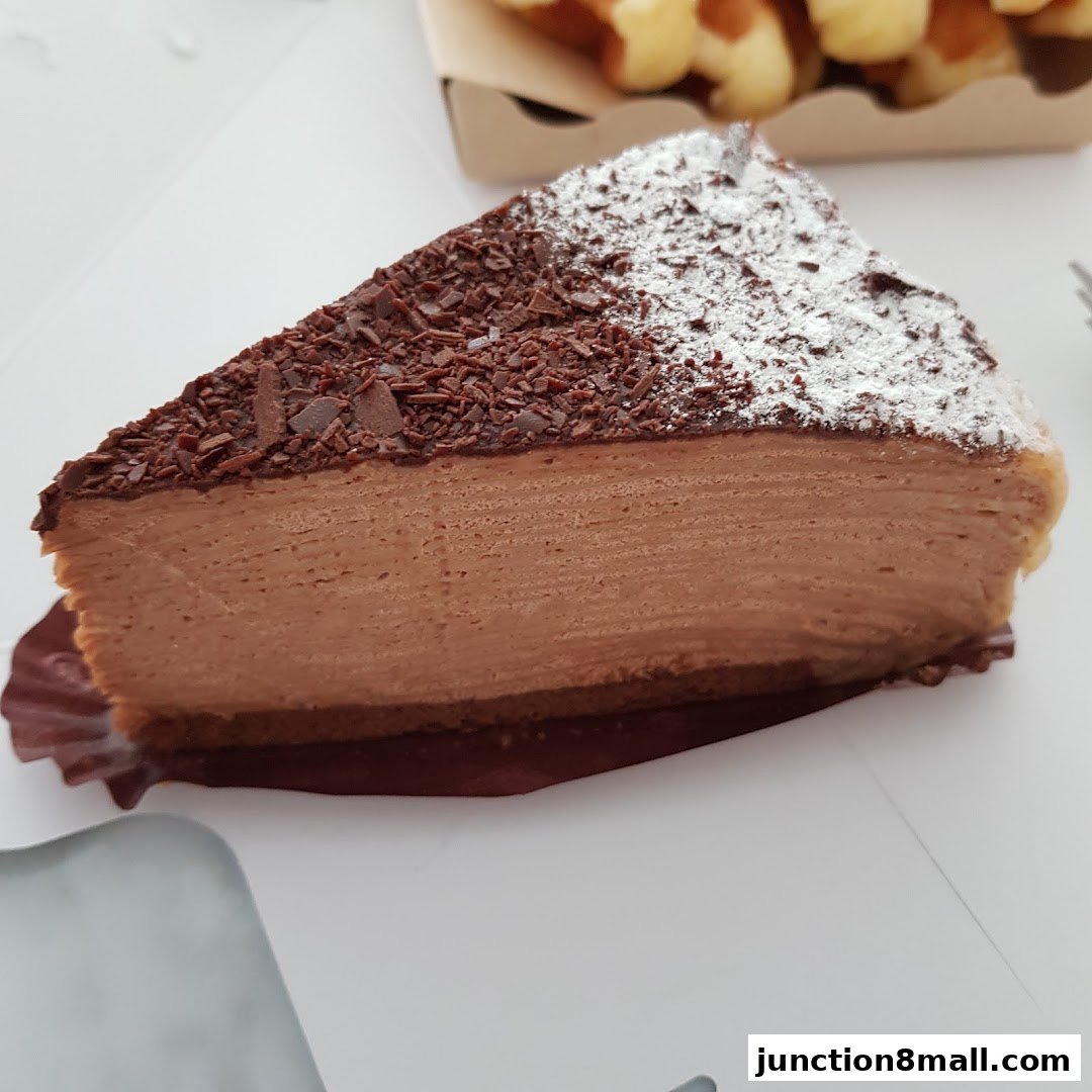 A slice of rich chocolate cheesecake topped with chocolate shavings and powdered sugar.