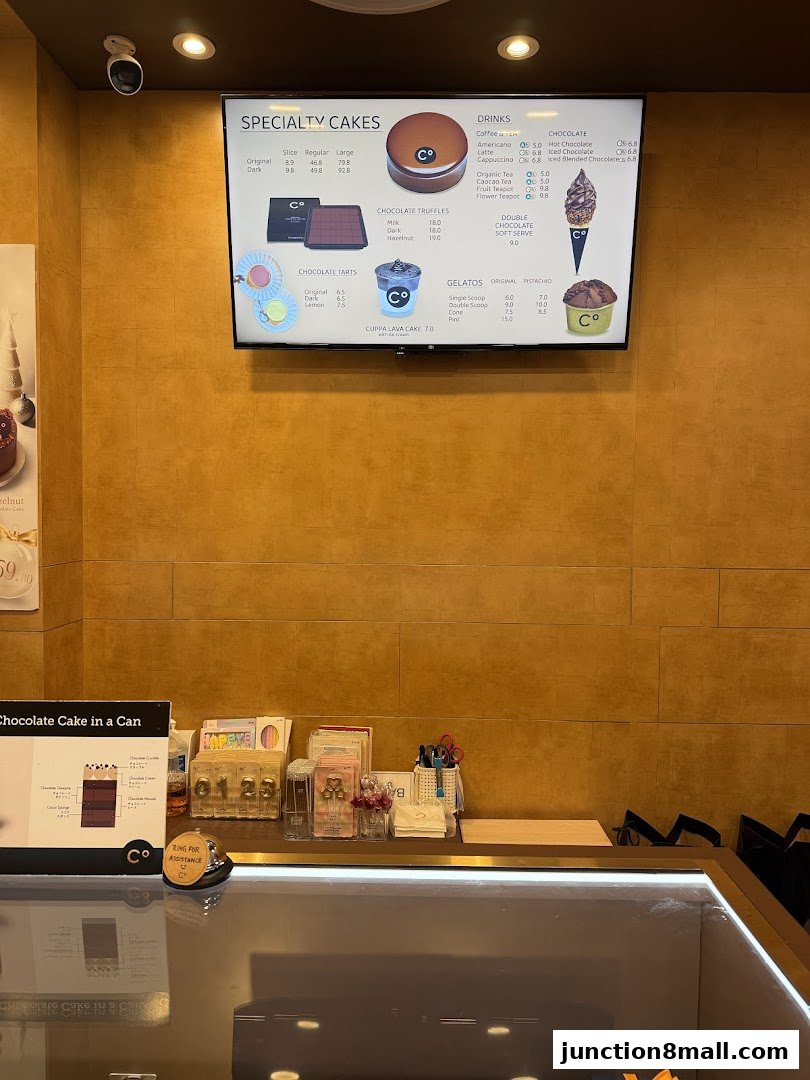 A digital menu board displaying specialty cakes, drinks, chocolate truffles, tarts, and gelato.