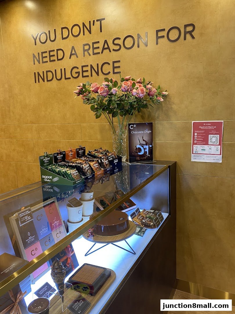 A display case filled with chocolates and cakes at Chocolate Origin, with a motivational quote on the wall.