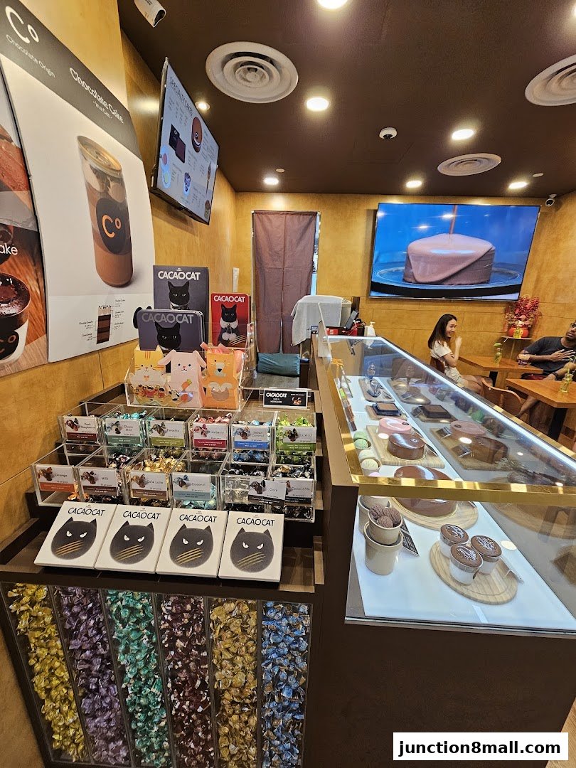 Interior of a chocolate shop with displays of chocolates, cakes, and seating area.