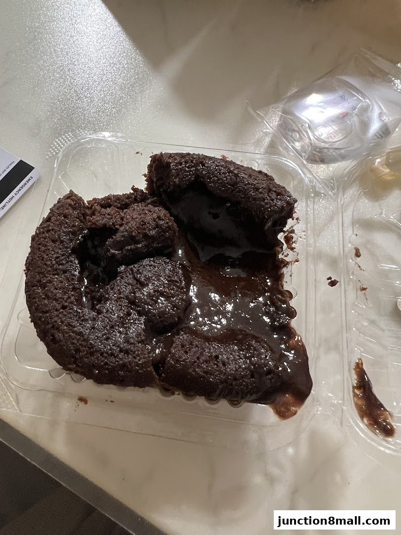 A decadent chocolate lava cake with molten chocolate oozing out, served in a clear plastic container.