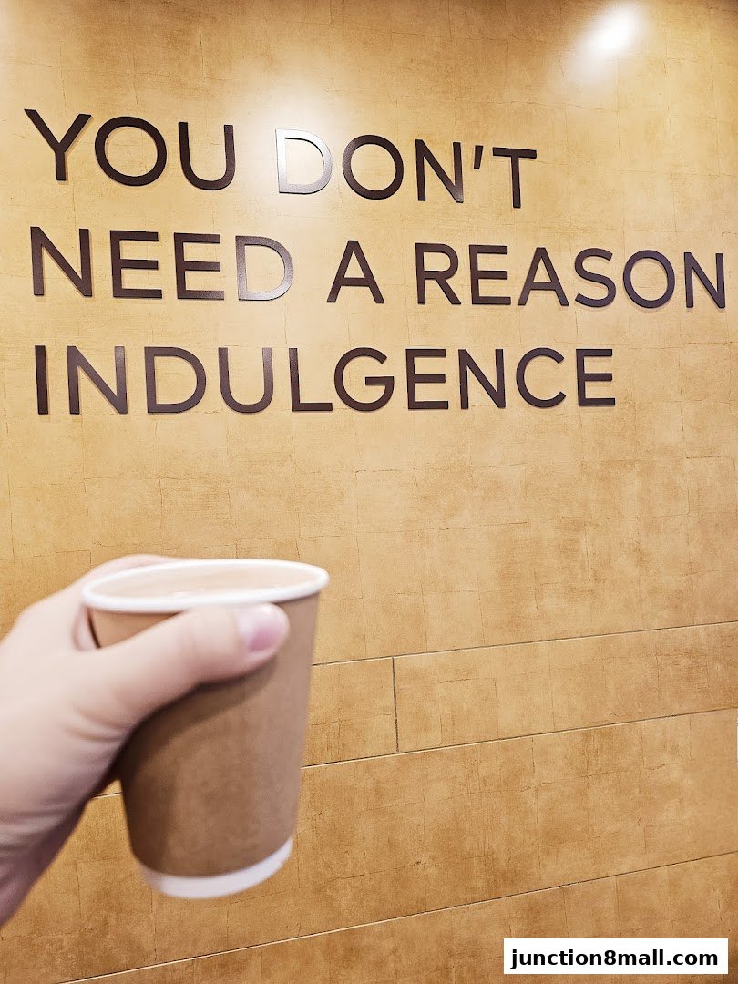A hand holds a cup of a beverage in front of a wall with text.