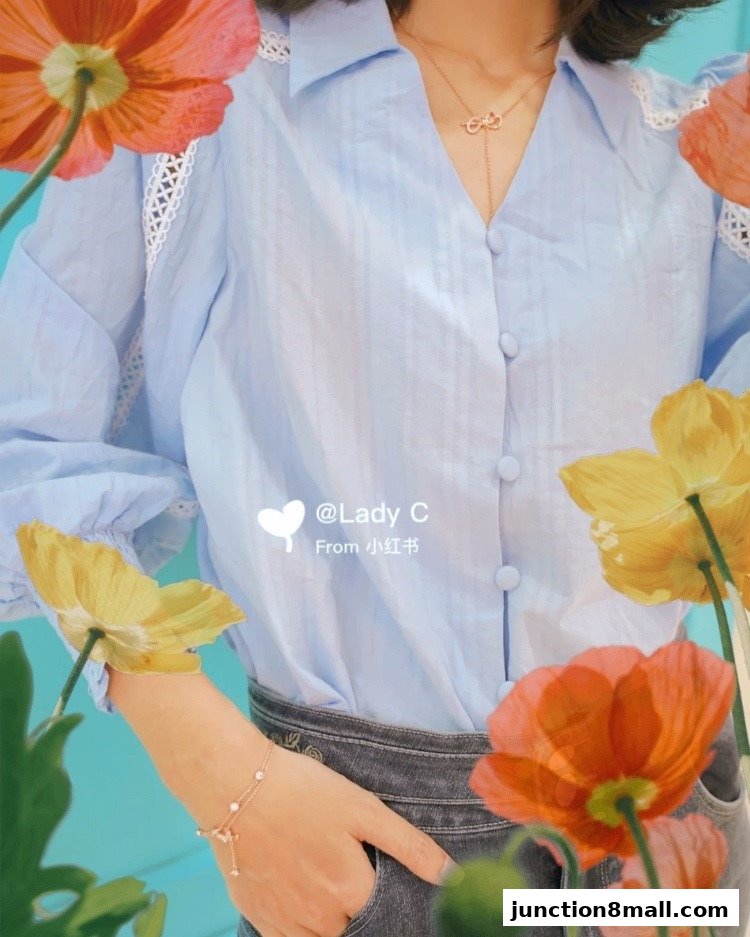 A person wearing a light blue blouse with lace details and a delicate necklace.