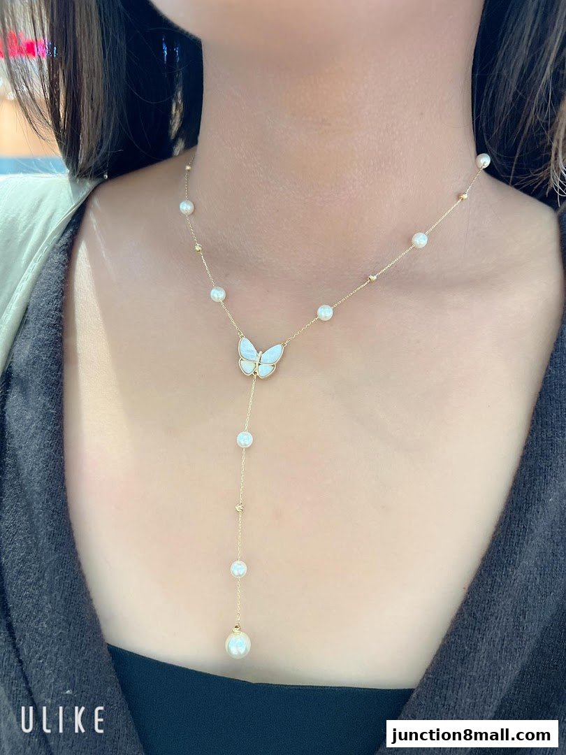 A woman wears a delicate gold necklace with pearls and a butterfly pendant.