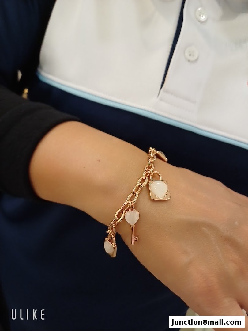 A close-up of a person's wrist wearing a rose gold charm bracelet with lock and key motifs.