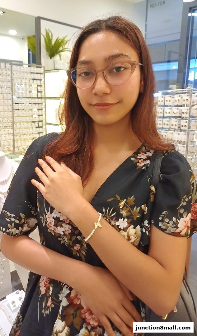 A young woman wearing glasses and a floral dress poses in a jewelry store.
