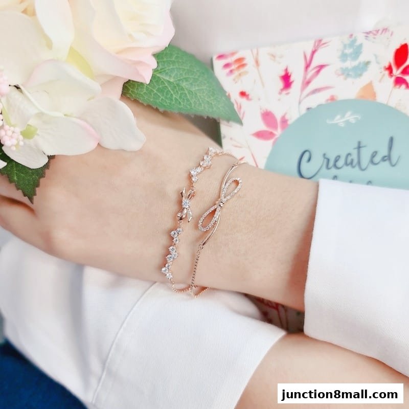 A hand wearing two delicate rose gold bracelets with sparkling stones and a bow.