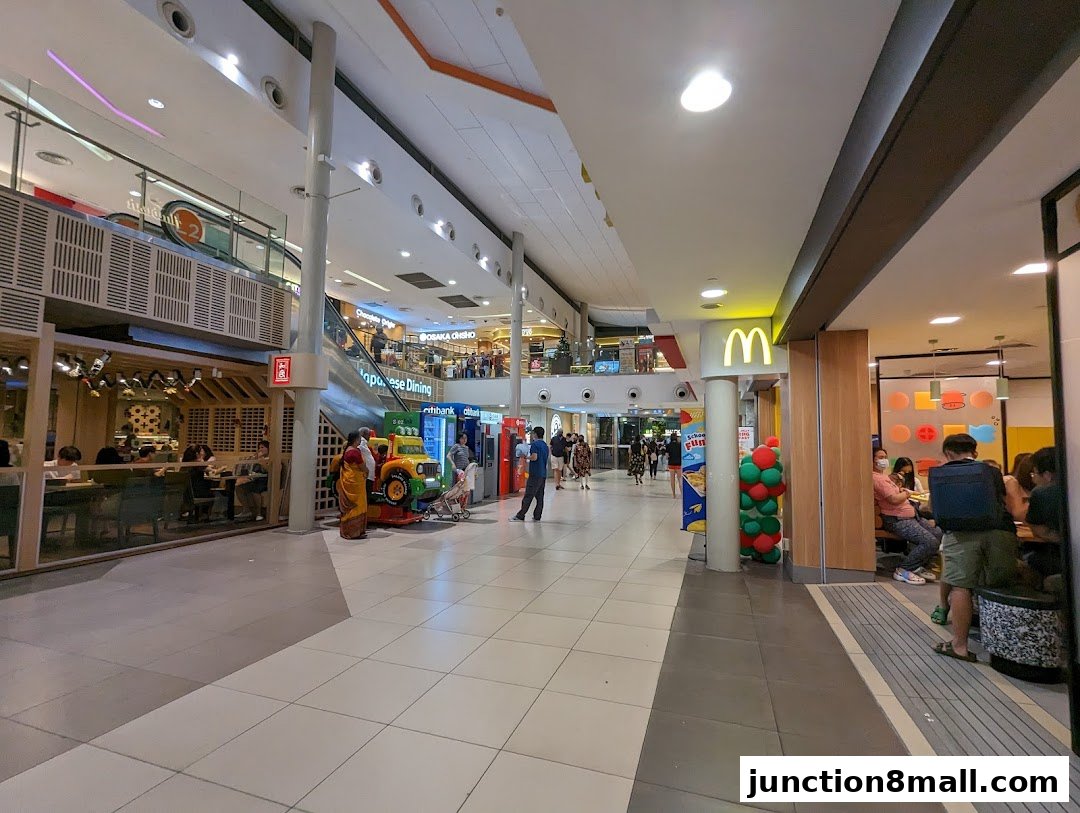 A busy shopping mall corridor with various shops and people walking.