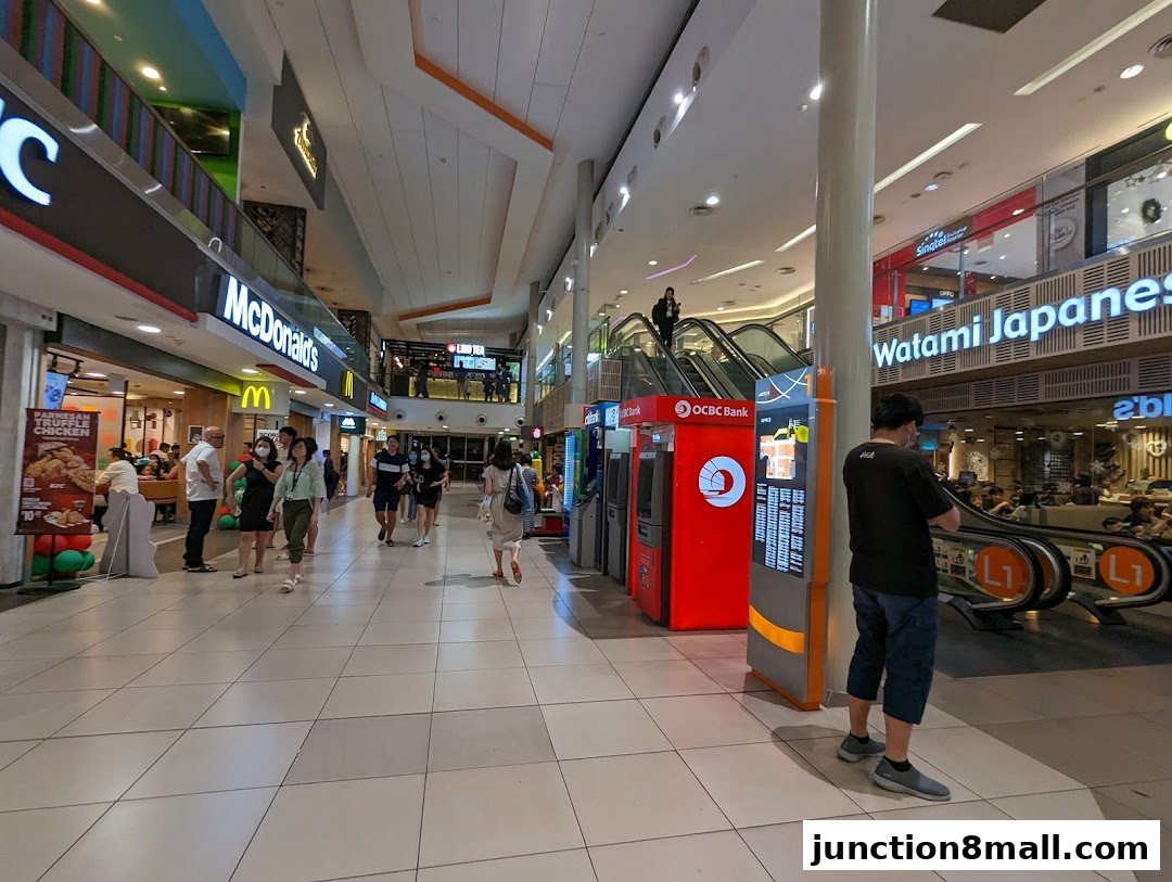 A busy shopping mall corridor with various shops, including McDonald's and Watami Japanese, and OCBC Bank ATMs.