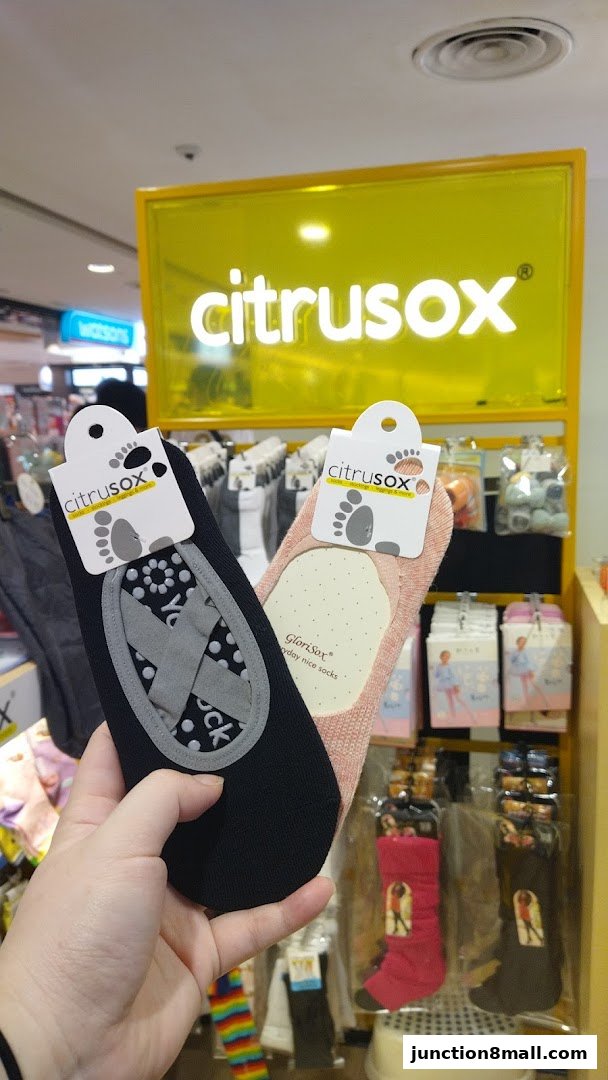 A hand holds two pairs of Citrusox socks in front of a display of socks.