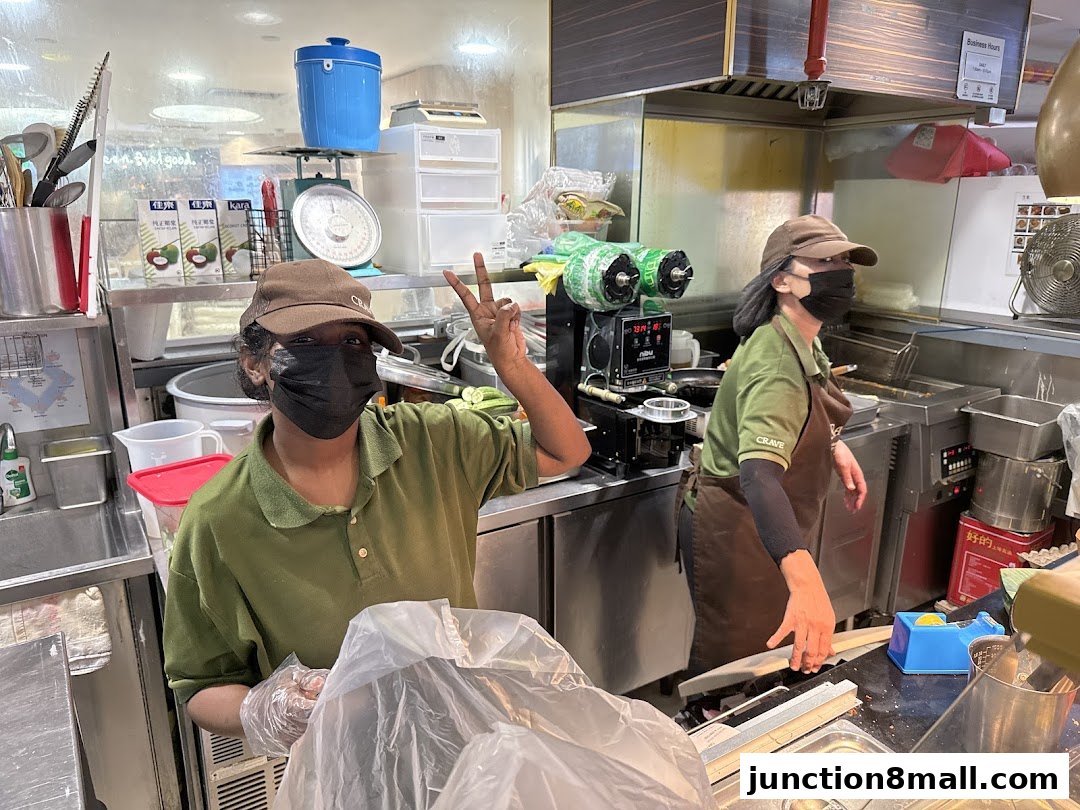 Two staff members in uniform are working behind the counter at a food establishment.