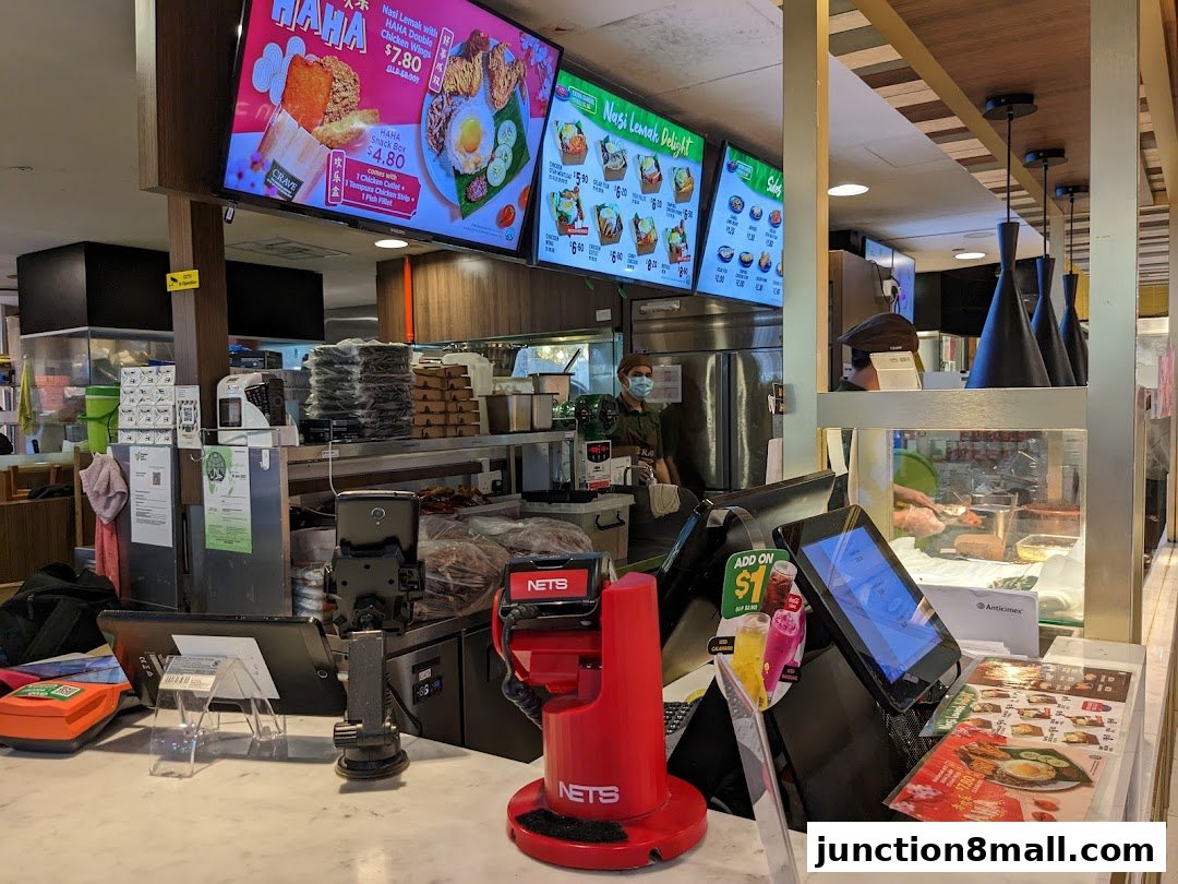A food counter with digital menus displaying Nasi Lemak dishes and a cashier area.