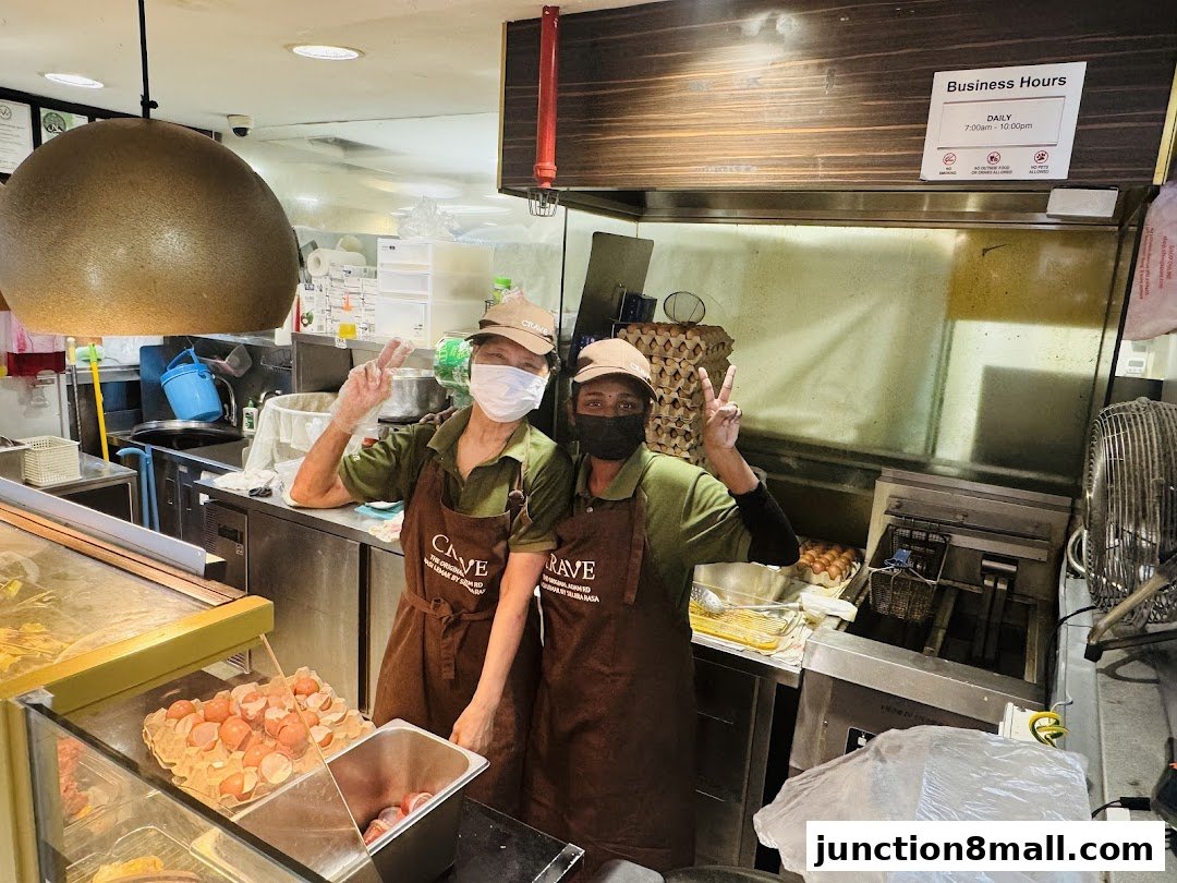 Two staff members in aprons pose with peace signs in a busy kitchen.