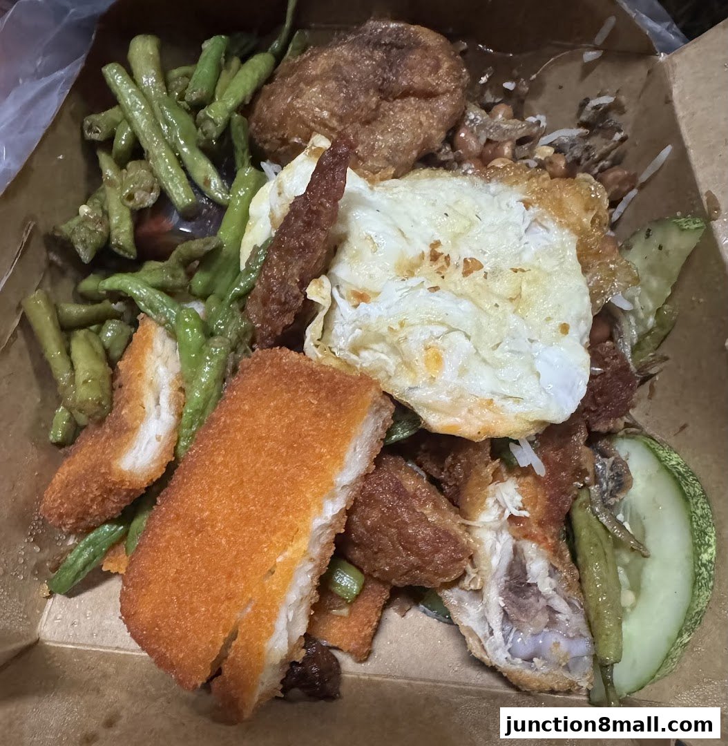 A close-up of a takeaway box filled with nasi lemak, featuring fried chicken, egg, and vegetables.