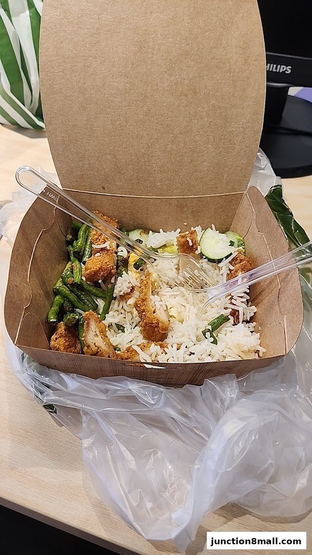 A takeaway box filled with nasi lemak, featuring rice, fried chicken, and green beans.