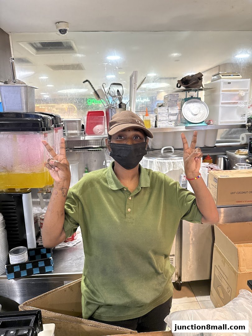 A staff member at Crave Nasi Lemak Junction 8 smiles and makes a peace sign.