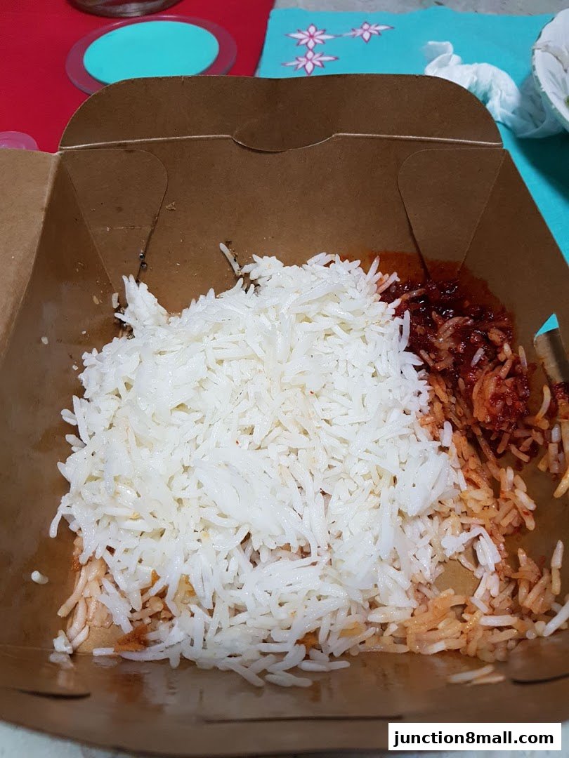 A close-up view of a takeaway box filled with nasi lemak, featuring white rice and sambal.