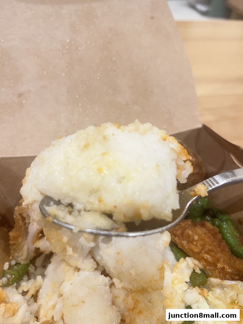 A close-up shot of a spoon scooping a portion of Nasi Lemak from a takeaway box.