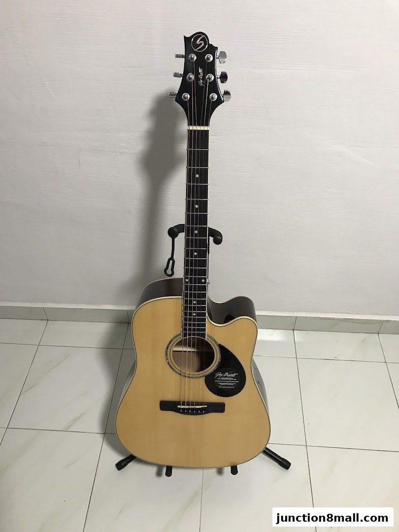 Acoustic guitar on a stand against a white wall.