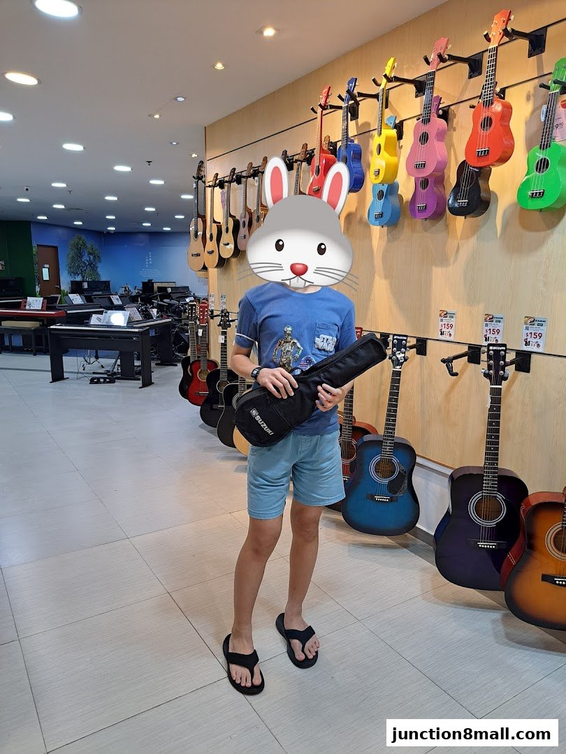 A person holding a guitar case in a music store with ukuleles and guitars on display.
