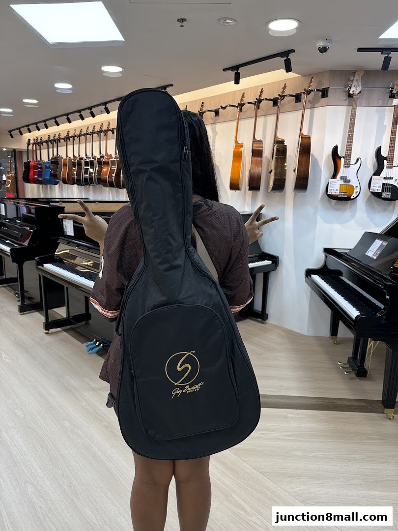 A person carries a guitar case in a music store with pianos and guitars on display.