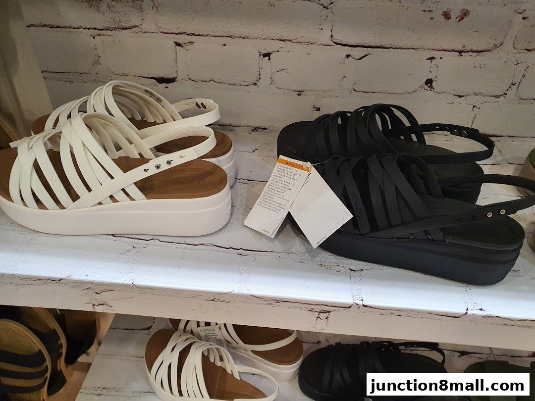 A display of white and black Crocs sandals on shelves with a brick-patterned background.