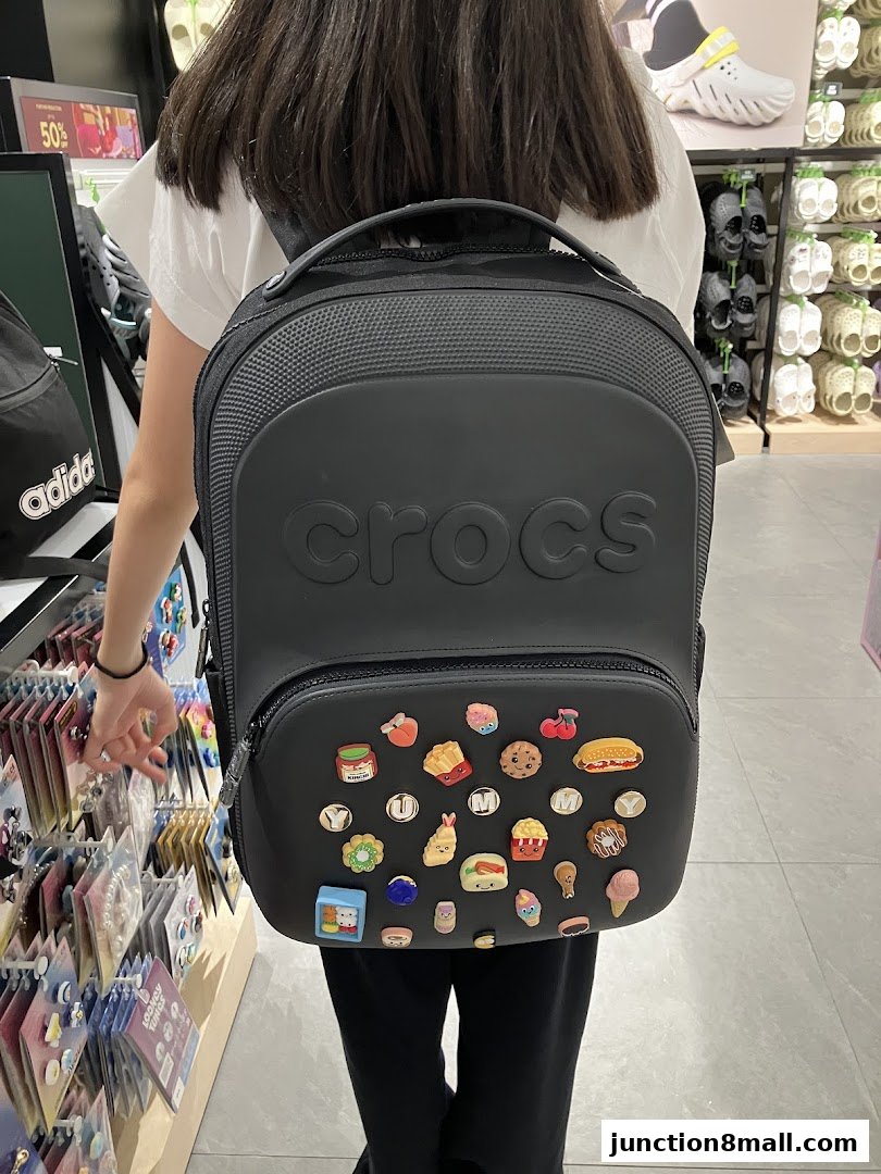 A person wearing a black Crocs backpack adorned with various food-themed Jibbitz charms.
