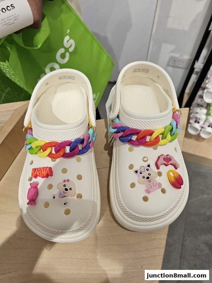 Two white Crocs shoes decorated with colorful charms and chains.