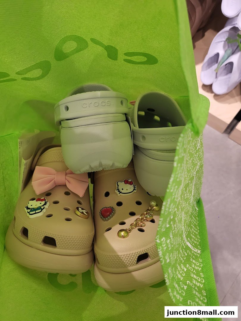 A bright green Crocs bag filled with light green and tan platform Crocs adorned with charms.