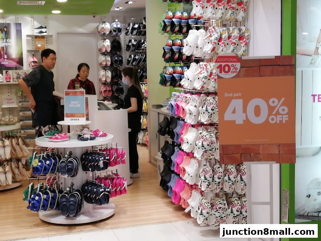 Interior of a Crocs store with various colorful footwear displayed and promotional signage.