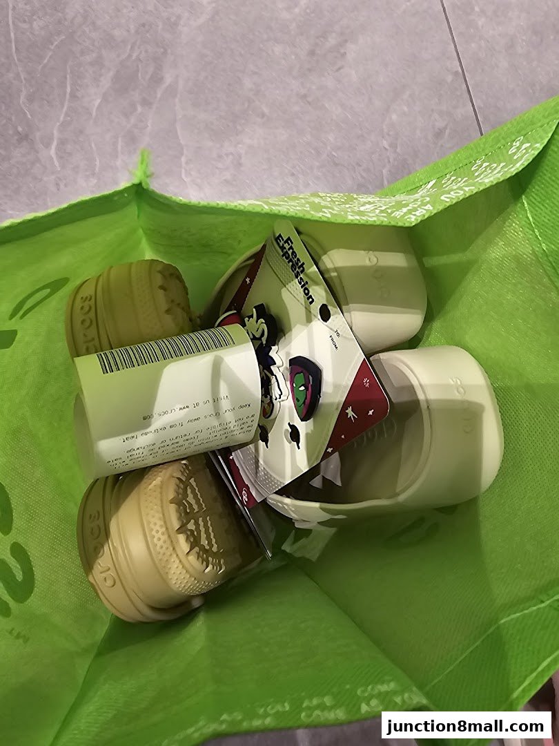 A bright green Crocs shopping bag filled with Jibbitz charms and shoe accessories.
