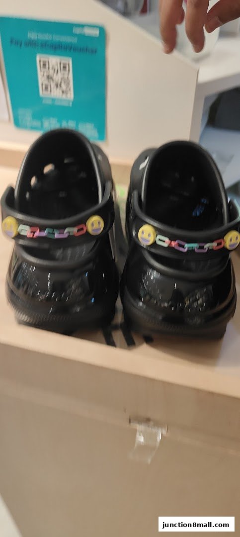 Close-up view of two black Crocs shoes with colorful smiley face charms.