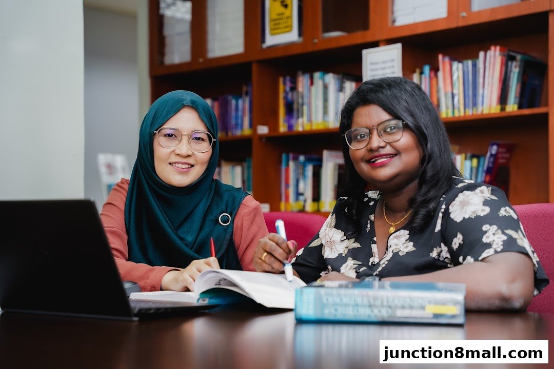 Two women smiling while studying at a table with books and a laptop.