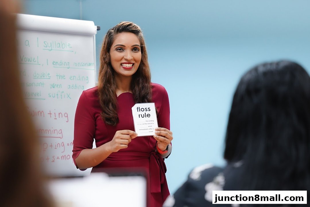 A smiling teacher holds up a flashcard in a classroom setting with a whiteboard.
