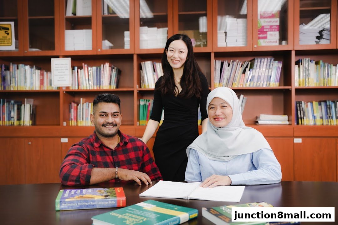 Three smiling individuals are seated at a table in front of bookshelves, with books on the table.