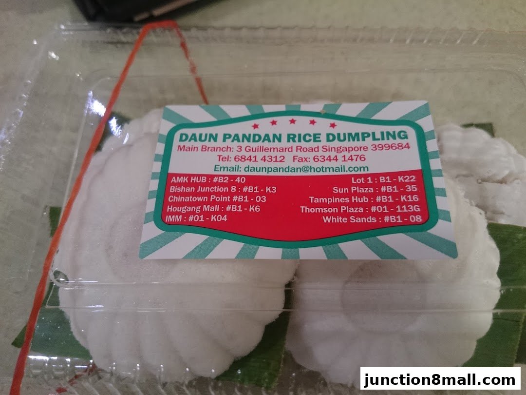 A clear plastic container holding two white rice dumplings with a business card from Daun Pandan Rice Dumpling.