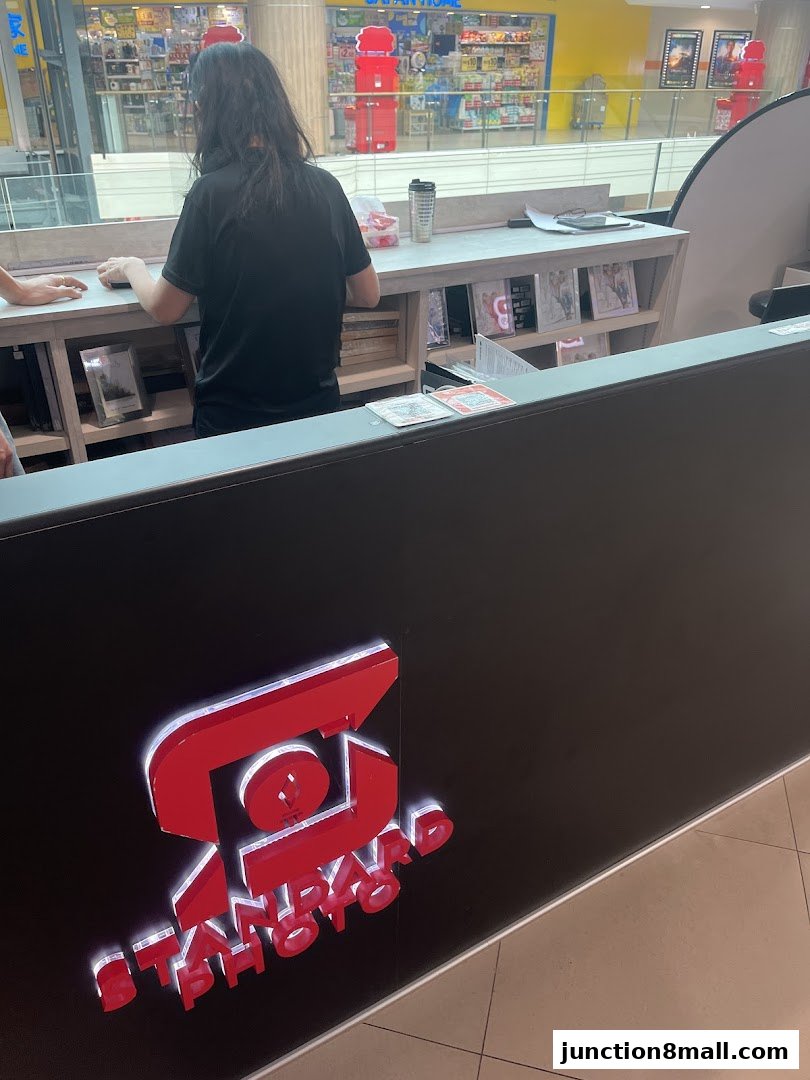 A person stands behind a counter with the "Standard Photo" logo, with retail displays in the background.