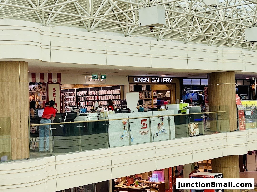 A view of various shops on an upper level of a shopping mall, including Standard Photo and Linen Gallery.