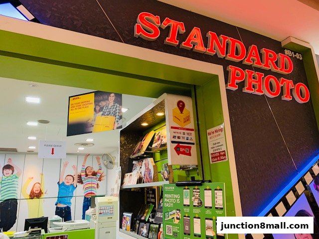 The entrance of Standard Photo, a DHL Express Service Point, featuring vibrant decor and promotional materials.