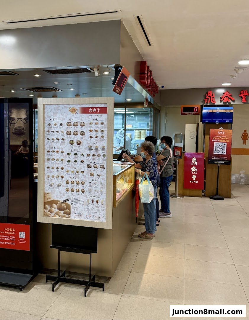 Customers queue at Din Tai Fung Junction 8, with a menu board displaying various food items.
