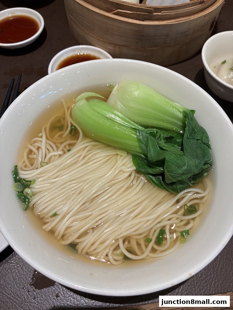 A bowl of steaming noodle soup with bok choy and a side of dipping sauce.