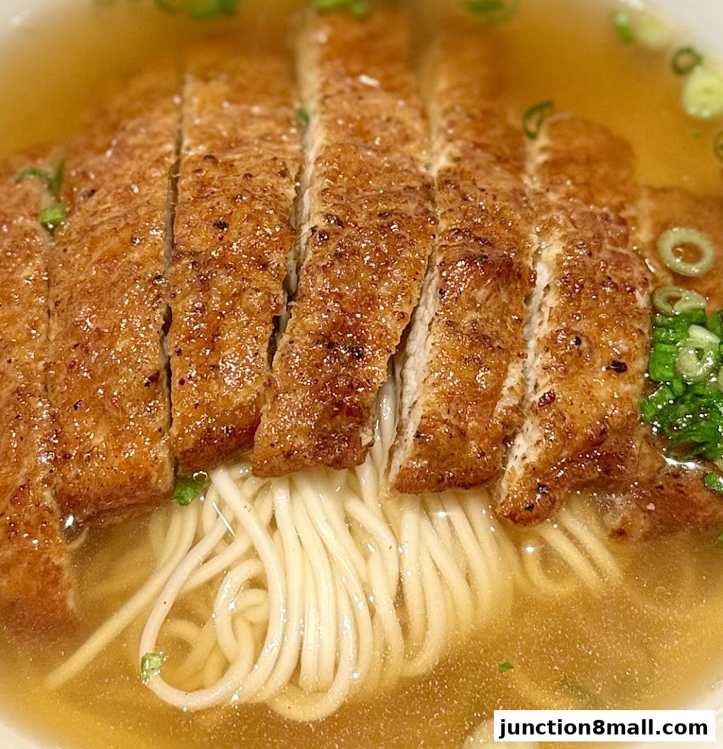 A close-up shot of a delicious bowl of noodles topped with sliced, crispy fried pork and garnished with green onions.