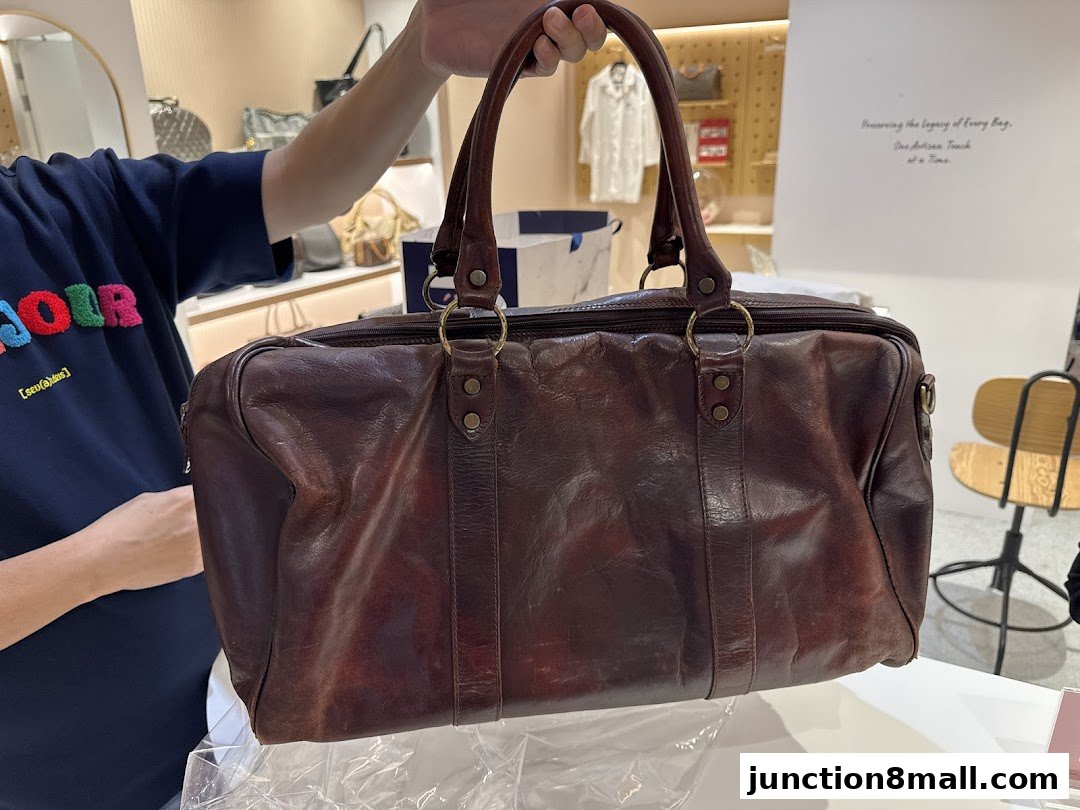 A person holds a large, dark brown leather duffel bag in a shop.