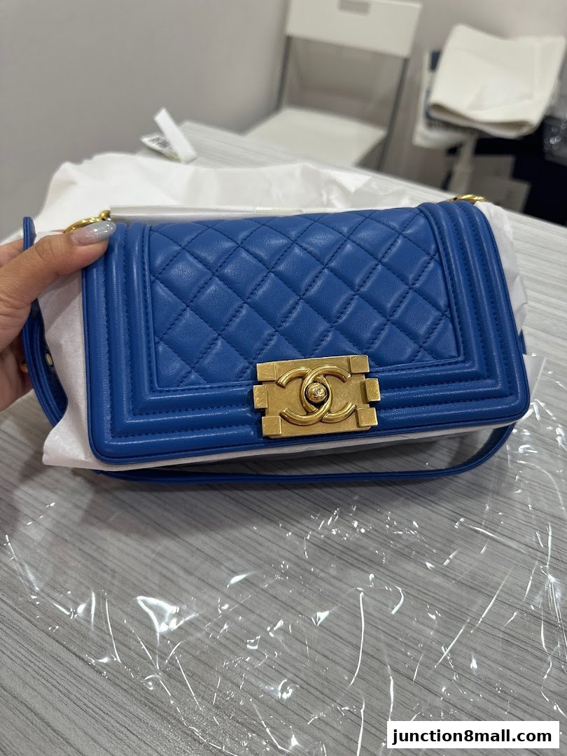 A hand holds a blue quilted handbag with gold hardware.