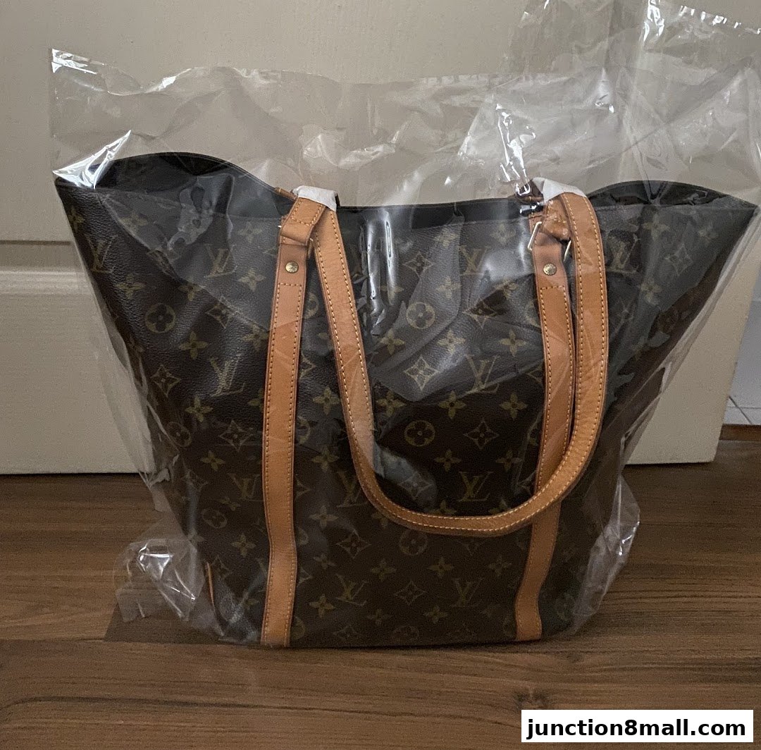 A classic monogram tote bag, wrapped in plastic, displayed on a wooden floor.