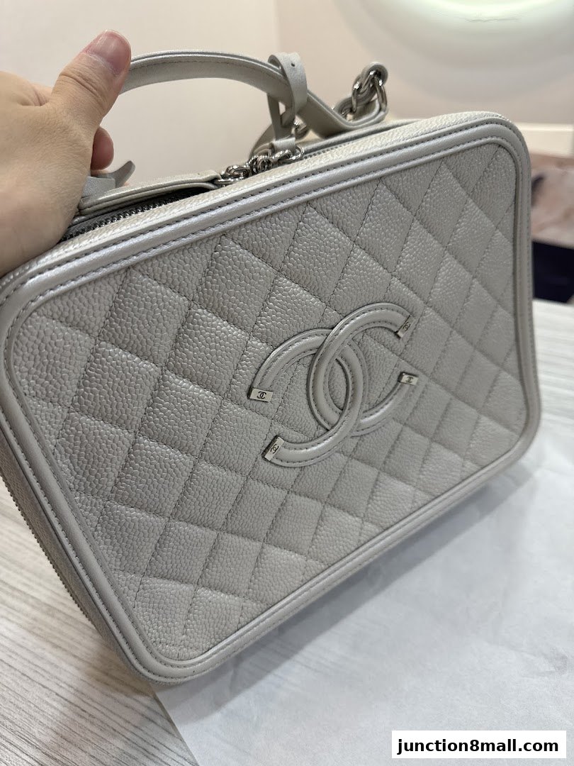 A hand holds a light grey quilted vanity case with a double C logo.