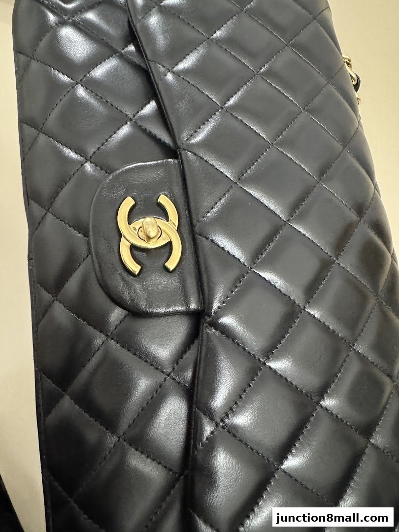 A close-up of a black quilted leather handbag with a gold interlocking logo.
