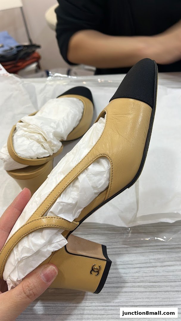 A hand holds a stylish beige and black slingback heel with a Chanel logo on the heel.