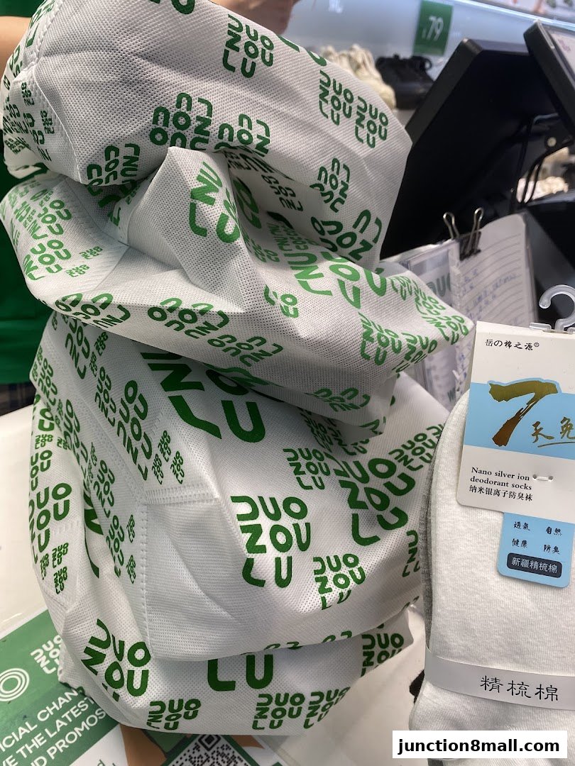 A pile of white fabric bags with green branding, next to a package of white socks.