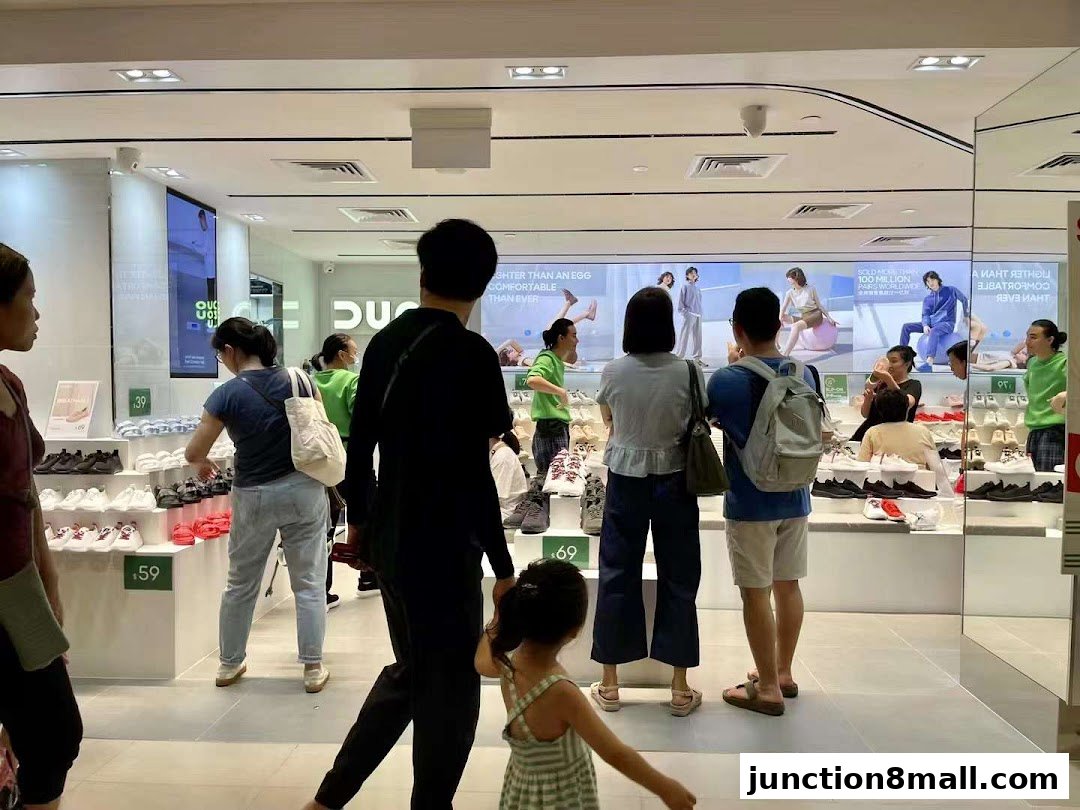 Shoppers browse a brightly lit shoe store with displays of footwear and promotional posters.